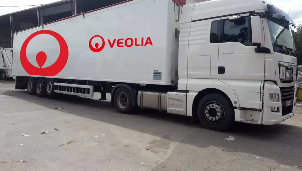 Das Bild zeigt einen weißen LKW mit rotem Veolia-Logo. Es handelt sich um einen Sattelschlepper mit Auflieger. Der LKW steht auf einer betonierten Fläche, dem Betriebshof von Veolia.