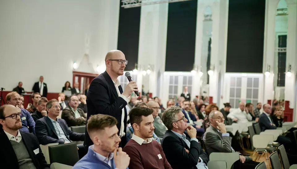Ein Teilnehmer am WasserDialog erhebt sich aus dem Publikum, hält ein Mikrofon in der Hand und stellt eine Frage