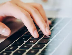 Nahaufnahme einer Hand, die auf der Tastatur eines Laptops schreibt.