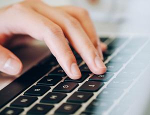 Nahaufnahme einer Hand, die auf der Tastatur eines Laptops schreibt.