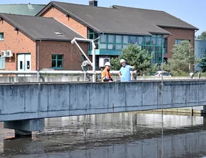Blick auf eine Kläranlage mit Räumerbrücke. Im Vordergrund befindet sich ein Klärbecken mit aufbereitetem Wasser. Auf der Brücke stehen zwei Veolia Mitarbeiter in Sicherheitskleidung. 