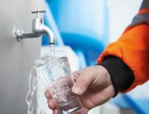 Nahaufnahme einer Hand, die ein Glas Wasser in der Hand hält. In das Glas wird Wasser gefüllt, was aus einem Wasserhahn kommt.