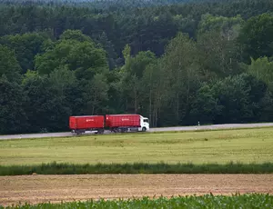 Luftaufnahme eines fahrenden weißen Veolia-LKW mit zwei roten Anhängern. Der LKW fährt auf einer Straße. Auf der linken Seite der Straße befindet sich ein Wald, auf der rechten ein Feld.