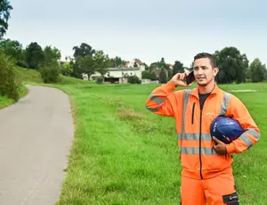 Veolia Mitarbeiter steht in Sicherheitskleidung an einer Landstraße und telefoniert