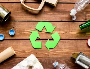 Das Recyclingzeichen auf hölzernen Grund umgeben von verschiedenen Abfällen