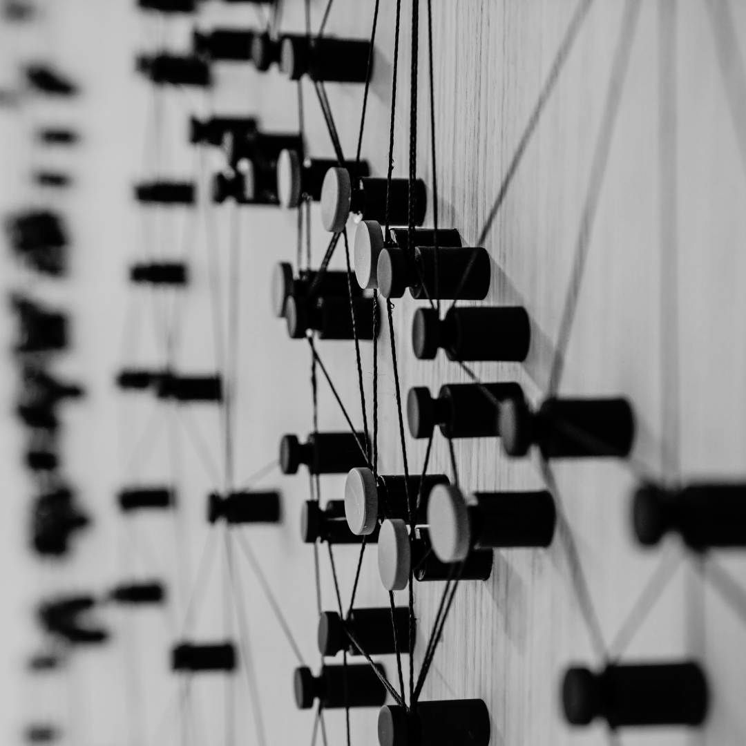 schwarz weiß Bild von Pins die in eine Wand gesteckt sind und mit Fäden verbunden