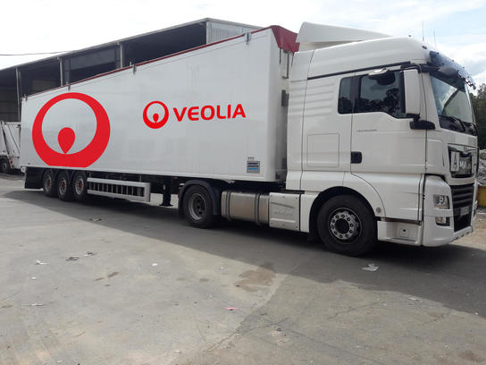 Das Bild zeigt einen weißen LKW mit rotem Veolia-Logo. Es handelt sich um einen Sattelschlepper mit Auflieger. Der LKW steht auf einer betonierten Fläche, dem Betriebshof von Veolia.