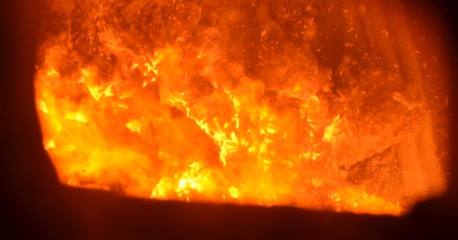 Das Bild zeigt das innere eines Hochofens. Man sieht eine massive, hell leuchtende Feuermasse in Orangetönen, die den gesamten sichtbaren Bereich ausfüllt. Die Hitze und Intensität des Feuers sind fast greifbar.