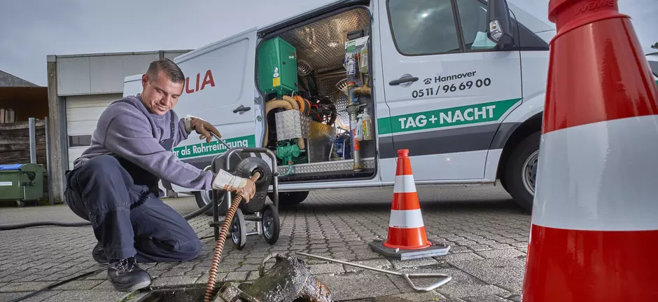 Aufnahme eines Mannes der einen Gullideckel aus dem Boden nimmt 