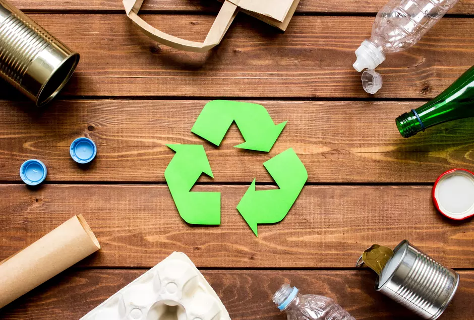 Das Recyclingzeichen auf hölzernen Grund umgeben von verschiedenen Abfällen