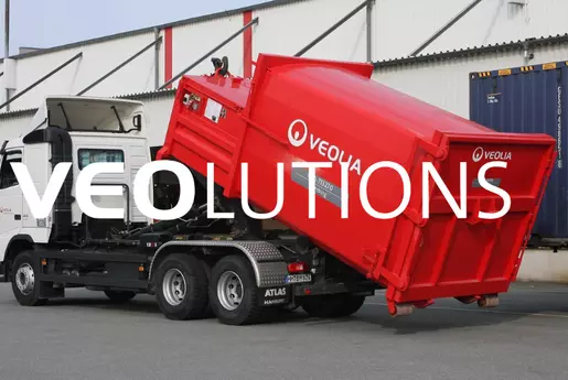 LKW lädt eine Presse ab, im Vordergrund dem Schriftzug Veolutions